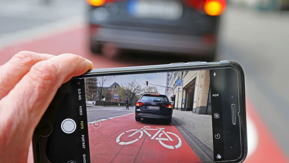 Die Foto-App auf einem Handybildschirm ist auf ein Autoa gerichtet, das auf dem Fahrradweg steht