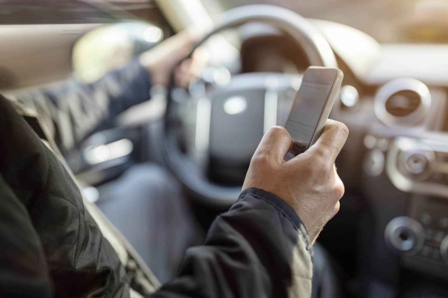 Ablenkung am Steuer: Ein Autofahrer schaut während der Fahrt auf sein Smartphone