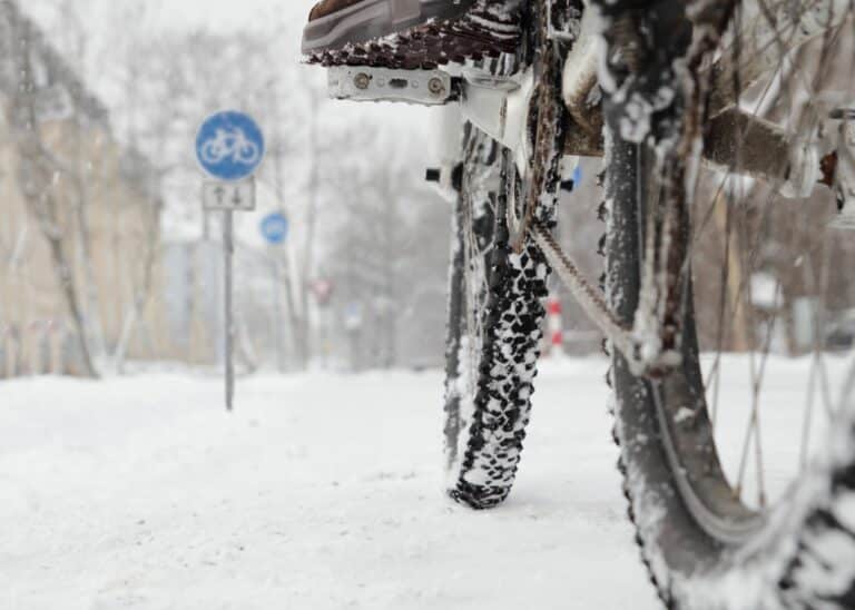 Fahrradfahren im Winter: ein Radfahrer steht mit seinem Rad auf einer verschneiten Straße